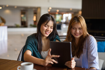 two women with tablet computer in cafe smiling