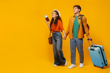 Happy couple with tickets and luggage walking on yellow backdrop, anticipating holiday adventure,...