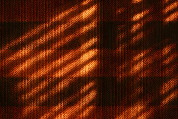 Diagonal shadows from window blinds falling across a red plaid wool textile, creating a warm textured pattern..