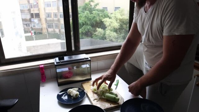 Chef cutting leeks and arranging on plate by kitchen window