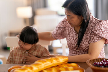 Caring mother gently comforts her child with Down syndrome at the dining table, creating a moment...