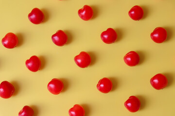 A concept of small red cherries spread out in a row. The contrast between the yellow background and the red cherries. The cherries are reminiscent of small hearts.