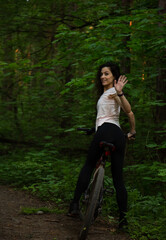 Beauty smiling sport woman biking on bicycle on path in a summer forest, looking back and waving...