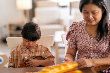 Caring mother gently comforts her child with Down syndrome at the dining table, creating a moment...