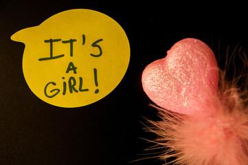 Photograph of a Yellow Emoji with “It’s a Girl” Text on Black Background