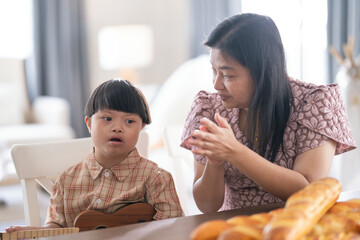 A child with Down syndrome playing ukulele while mother claps along, encouraging musical...