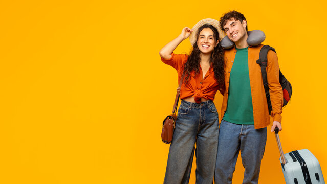 Portrait of happy European couple traveling, ready for vacation, posing with suitcase on yellow background