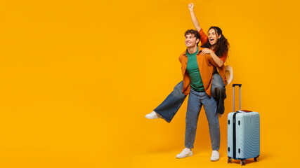 Excited European couple having fun, standing with suitcase on orange background, panorama with free space for design, banner