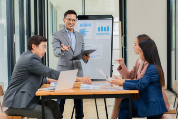 Group of Asian business people discussing charts and graphs showing the results of successful business investment and growth showing the results of successful teamwork.