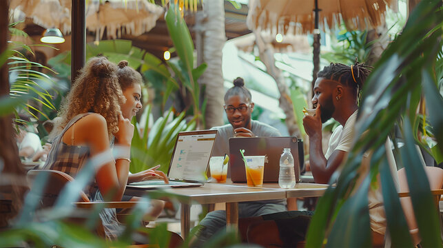 Group of young multicultural digital nomads working on laptops in an open-air café with tropical plants and iced drinks. Summer remote work, freelancer lifestyle, digital lifestyle in summer