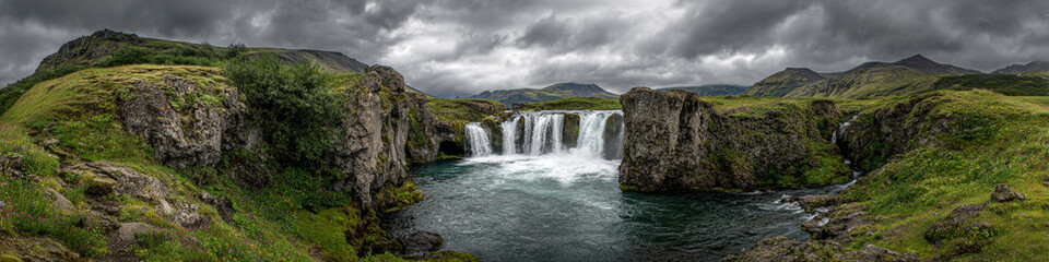 Obraz premium Panoramic view of a scenic waterfall flowing between rocky cliffs under a cloudy sky landscape view
