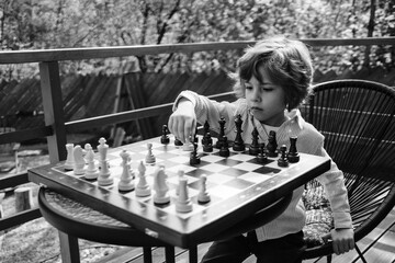 Preschool child learning to play smart board game chess. Boy moves pawn piece