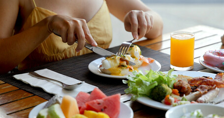Person enjoying healthy breakfast with eggs Benedict, salad, fruit, and orange juice at outdoor...