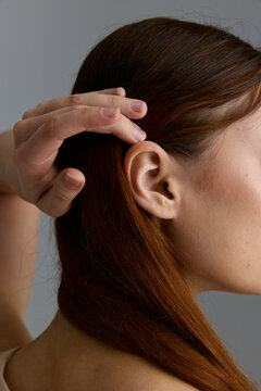 Beauty woman with smooth auburn hair gently holding strands near ear, showcasing natural texture and minimalistic style in soft studio lighting.