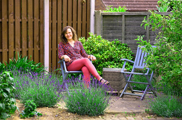 Woman sitting on a wooden chair, relaxing in her lavender garden.