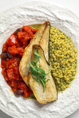 Portion of coooked sea bass fillet with ptitim tomatoes and olives