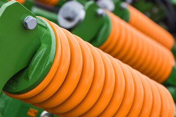 Orange hard spring made of steel. Part of big industrial or agricultural machine