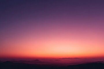 Fototapeta premium Vibrant sunset hues paint a hazy, mountainous landscape, transitioning from deep purple to fiery orange at the horizon
