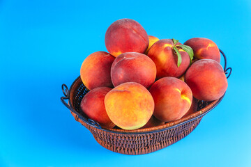 Woven basket overflows with fresh peaches, showcasing their rich colors natural beauty on blue background.