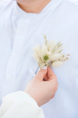 Man in white shirt receives a flower boutonniere from a hand