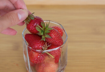 Hand holding a strawberry from cup full of the same fruit.