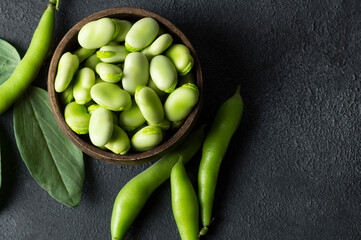 Fresh broad beans with pod in bowl on dark rustic background, healthy food