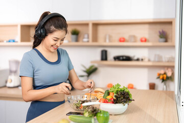 ESG and Culinary Joy. Woman preparing a fresh salad in the kitchen while listening to music.