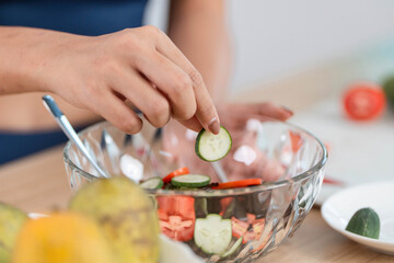 ESG and Salad Preparation. Woman adding cucumber slices to a fresh vegetable bowl.
