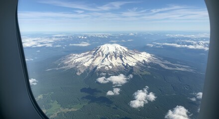 Aerial view of a snow-capped mountain peak, partly obscured by clouds, from an airplane window. Lush green valleys and distant mountains are visible
