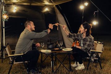 A man and a woman are sitting at a table with plates of food in front of them. They are eating spaghetti and drinking wine. camping outdoor lifestyle concept.