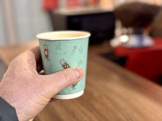 A hand is holding a warm cup of coffee in a contemporary cafe setting filled with aroma and style. A hand gently cradling a warm, steaming coffee cup, showcasing a cozy and inviting cafe ambiance