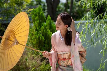 Young Japanese woman dressing in traditional kimono or yukata costume holding yellow umbrella in...