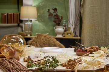 Flat lay composition showing natural materials for making a dried flower wreath. Includes dried flowers, grasses, twine, scissors, floral wire, and a round base frame arranged on a rustic linen-covere