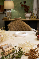 Flat lay composition showing natural materials for making a dried flower wreath. Includes dried flowers, grasses, twine, scissors, floral wire, and a round base frame arranged on a rustic linen-covere