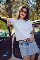 Young woman in white t-shirt and denim skirt standing by car