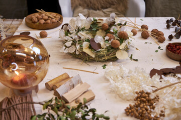 Flat lay of a completed handmade dried flower wreath placed on a bright wooden table, surrounded by crafting materials like dried flowers, twine, scissors, and floral wire. The natural light and soft 