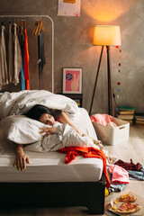Young woman sleeping in messy bedroom after party