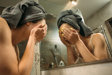 Young woman washing face in bathroom sink after party