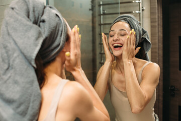 Happy woman washing face in bathroom mirror after party