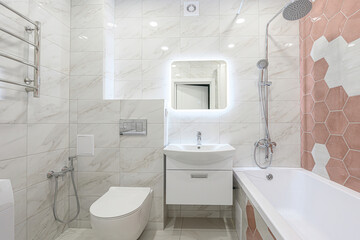 Bright bathroom featuring white marble-patterned tiles, hexagonal accent tiles, a toilet, sink with...