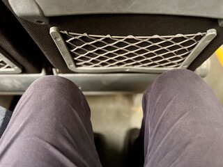 Two passengers are sitting in an armchair with a narrow footway in the economy class cabin of the bus. View of the legs from above. People in transport, close-up