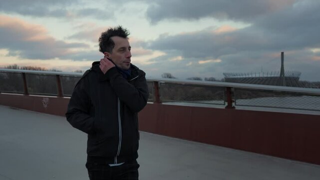 A man protects himself from more than just the weather. On a cold city bridge, he wraps his scarf tighter, a gesture of seeking comfort from urban alienation and inner loneliness.