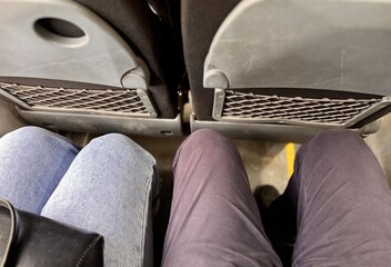 Two passengers are sitting in an armchair with a narrow footway in the economy class cabin of the bus. View of the legs from above. People in transport, close-up