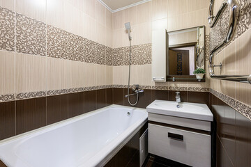 well-lit bathroom with a white tub, patterned beige and brown tiles, a vanity sink, and a mirror