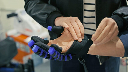 Person assisting with wearable robotic rehabilitation glove. Close-up of a person fitting a high-tech robotic rehabilitation glove with blue finger actuators onto another person's hand.