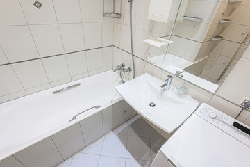 Bright, clean bathroom featuring white tiles, a bathtub, sink, and a mirrored cabinet