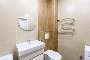 Modern bathroom featuring a sink, round mirror, toilet, and heated towel rack, all against tiled walls