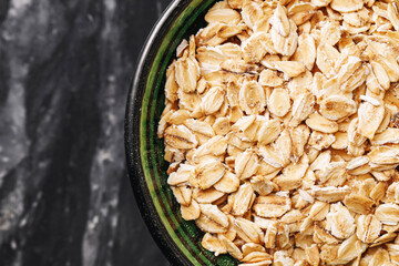 Raw oats in black bowl. Healthy organic grain for breakfast. Top view on marble table. Rustic natural background. Vegan dietary fiber source. Clean eating concept. Natural whole grain.