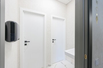 bright restroom area with two white doors, a black hand dryer, and a woman's restroom sign