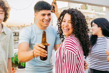 Young Latin couple, smiling, hugging and looking at the camera at party with friends on terrace